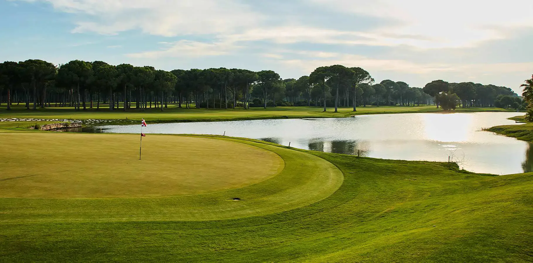 A lake-side green on Gloria Old Course surrounded by mature pine trees